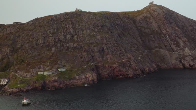 Steep rocky point creates a protected port in St. John's. Navigational marker protects ships entering harbor. High aerial view of Eastern Canada landscape.