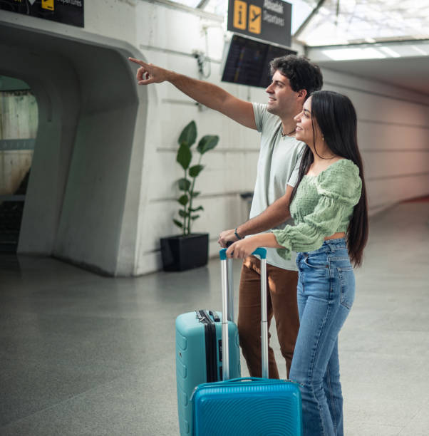 istock multicultural latin couple at airport with luggage looking at flight board 1996229372