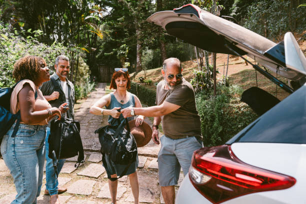 Two smiling mature couples unpacking their bags from the trunk of a car after arriving at their weekend vacation accommodation