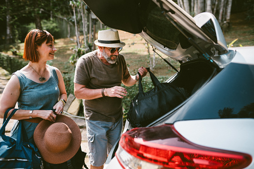 Smiling mature couple unpacking their luggage from the trunk of their car while after arriving for a weekend getaway