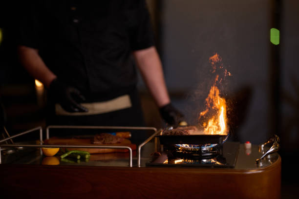Peruvian chef flambéing fish in a wok, creating high flames and smoke in a professional kitchen