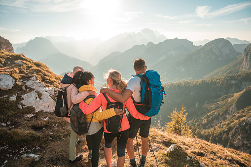 A diverse group embraces and has fun during their sunny day hike through the Julian Alps, taking in the beautiful views in the distance.