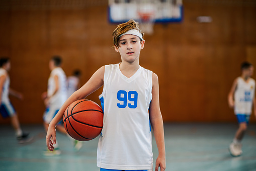Portrait of a male teenager holding a basketball in an indoor court.