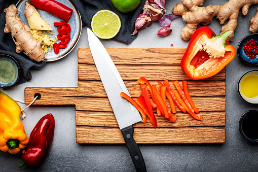 Food and cooking background. Wooden cutting board with chopped paprika and chef knife. Zucchini, raw vegetables, spices and ingredients for cooking vegan Asian dishes with ginger, garlic, soy sauce, top view