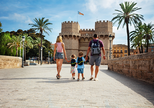 Parents with two kids walk in sunny Valencia in front of famous Torres de Serranos during their summer holidays in Spain, view from behind