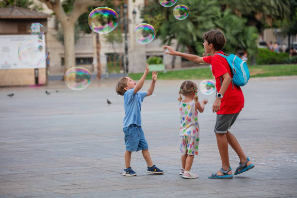 Group of children play and try to catch the huge soap bubbles at summer day on the city square in Valencia, Spain
