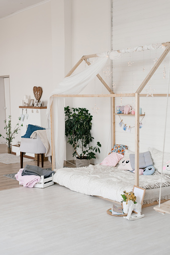 Children's stylish bed in the form of a house. Scandinavian style bedroom with grey pillows. Cozy children's bedroom in Scandinavian style