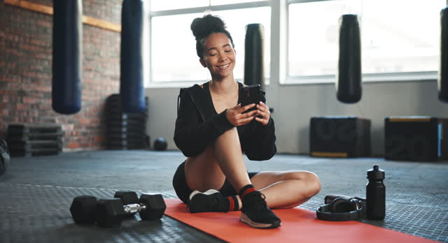 Gym, fitness and woman with a smartphone, typing and smile with workout, connection and exercise. Person on the floor, health or girl with a cellphone, mobile app and meme with social media and relax