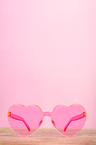 A cute pair of plastic heart shaped sunglasses on a pink background.