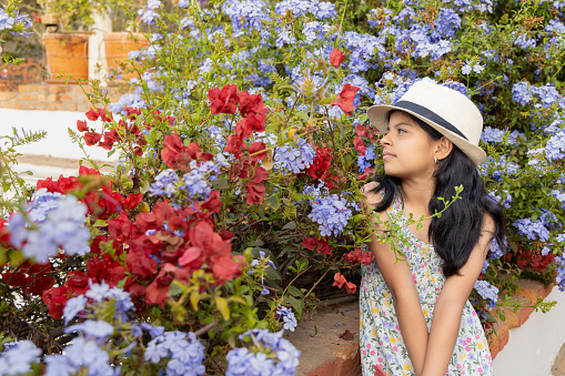 Little latin girl with straw hat and dress in a flower standing garden