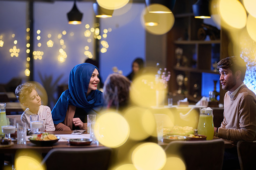 In a modern restaurant, an Islamic couple and their children joyfully await their iftar meal during the holy month of Ramadan, embodying familial harmony and cultural celebration amidst the contemporary dining ambiance.