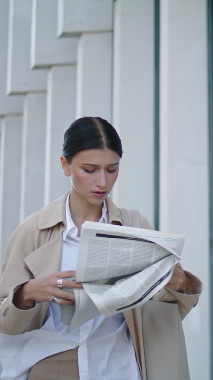 Busy woman reading newspaper going for work. Lady walking with press vertically