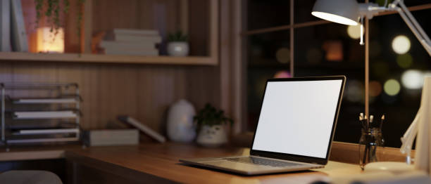 istock Modern and cozy home office workspace at night with a white-screen laptop computer on a wood table. 1996639161