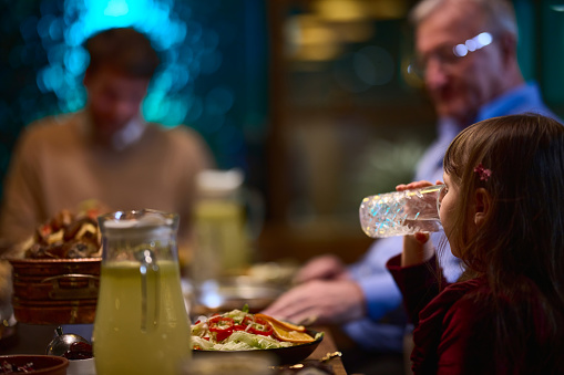 In a modern restaurant, a young girl participates in iftar by breaking her fast with water, embodying the tradition and significance of Ramadan in a contemporary setting