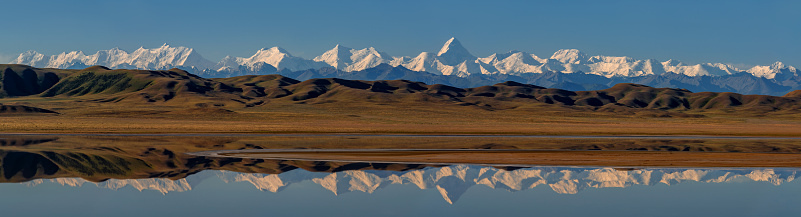 Mountain range of the Northern Tien Shan with the Khan Tengri and Pobeda Peaks and their reflection in the Tuzkol mountain lake on a summer morning