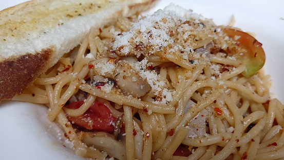 Delicious spaghetti aglio e olio with crusty bread on a white plate.