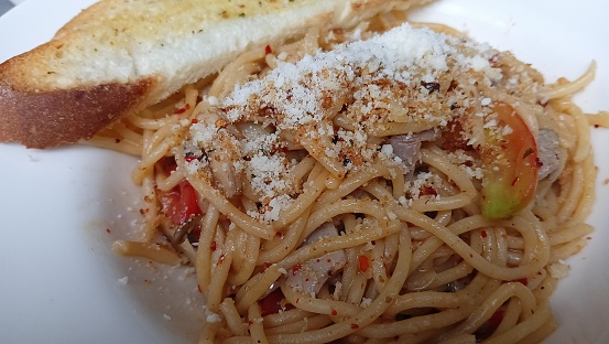 Delicious spaghetti aglio e olio with crusty bread on a white plate.