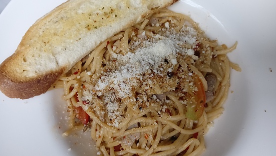 Delicious spaghetti aglio e olio with crusty bread on a white plate.