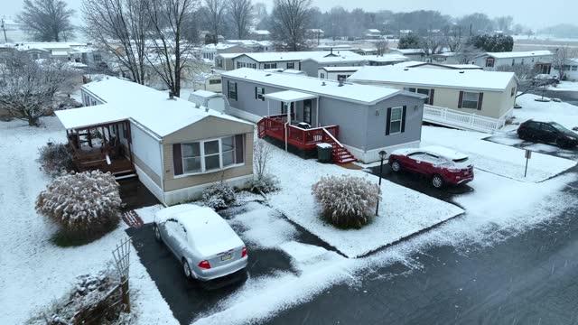 Mobile home with snow falling in USA. Low income houses. Manufactured housing. Aerial during snow storm in winter.