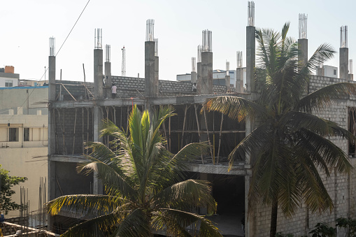 Hassan, Karnataka, India - January 10 2023: This image depicts the ongoing construction of a multi-story building with a foreground of natural greenery.