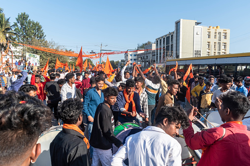 Hassan, Karnataka, India - January 10 2023: A large group of Bajrang Dal participants march down a bustling street with flags during a daytime procession.