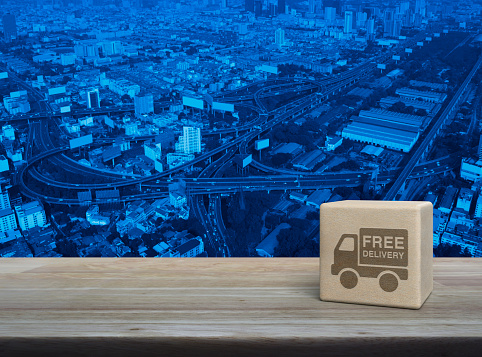 Free delivery truck icon on wood block cube on wooden table over modern city tower, street, expressway and skyscraper, Business transportation service concept