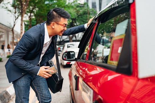 Young Chinese businessman in the streets of downtown Kuala Lumpur stopped a typical generic Kuala Lumpur Taxi, smiling and chatting with the cab driver where to go. Kuala Lumpur, Malaysia, Asia