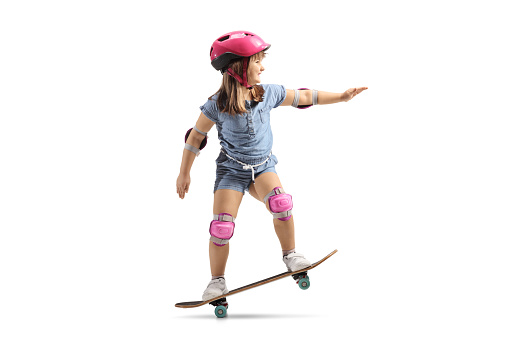 Little girl riding a skateboard with helmet, knee and elbow pads isolated on white background