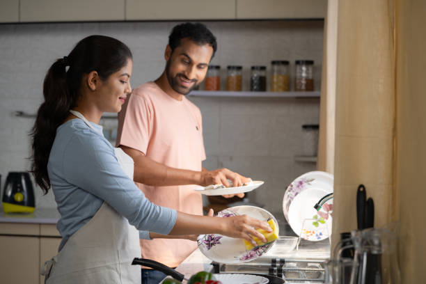Relaxed indian couples washing dishes together at kitchen during weekend - concept of sharing housework, spending time together and relationship caring