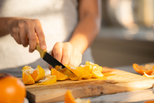 Close up shot of woman slicing oranges of making juice at morning in kitchen - concept of healthy lifestyle, nutrition and refreshing