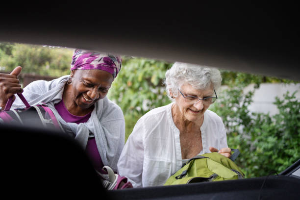smiling senior women packing bags into their car trunk for a road trip - active seniors enjoyment driveway vitality imagens e fotografias de stock