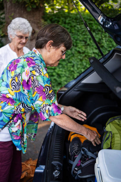 deux femmes âgées emballent des sacs dans le coffre d’une voiture pour un voyage en voiture - active seniors enjoyment driveway vitality photos et images de collection