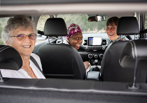 Portrait of a group of senior women looking over their shoulder's and smiling while sitting in a car during a road trip together