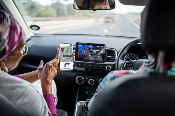Senior woman sitting in the passenger seat of a car and checking a map app on her smart phone during a road trip with friends