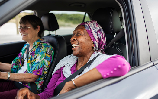 Senior women laughing while sitting in the passenger seat of a car during a road trip with a friend