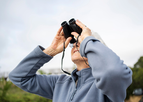 Smiling senior woman looking at something through binoculars during a walk outdoors in summer