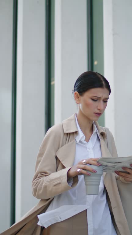 Businesswoman walking reading newspaper on street. Girl holding press vertically