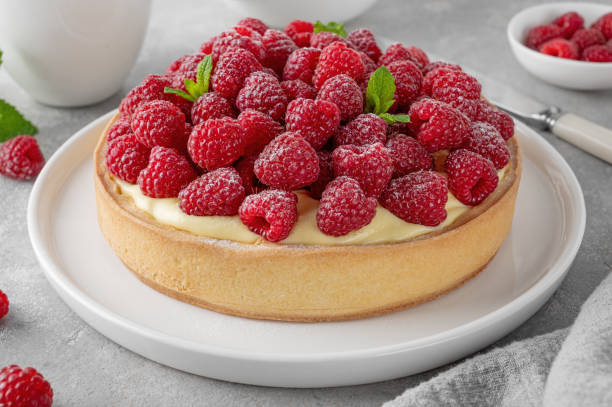 istock Delicious raspberry tart with vanilla custard cream sprinkled with powdered sugar on a white plate on a gray concrete background. Summer dessert. 1997082785