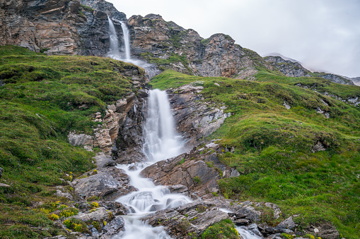 waterfall between alpine pasture high up in european mountains on cold summer day with clouds long exposure