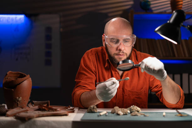 istock Restorer working late at night in the office restoring ancient coins. Restorer, conservation. Archaeological 1997094729