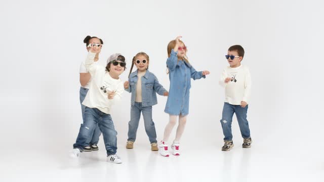 A group of modern, happy children are dancing and having fun on a light isolated background. Concept for clothing advertising, children's shopping and style.