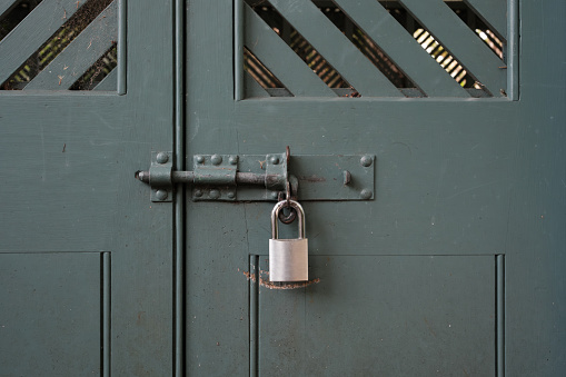 Silver padlock on a bolt, locking a green wooden door.