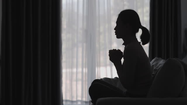 Silhouette of a women is praying to God in the morning room. Praying hands with faith in religion and belief in God on blessing background. Power of hope or love and devotion.