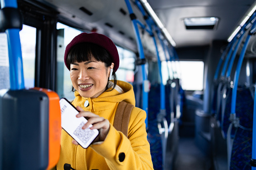 Beautiful woman passenger using her phone to validate digital ticket inside public bus transportation.
