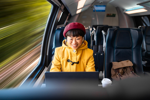 Woman traveling by high speed train while working on laptop computer in comfortable first class seat.