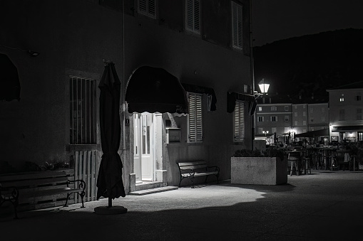 Cres, Croatia - October 24, 2022: Narrow street of Cres in the night, entrance to a house, black and white