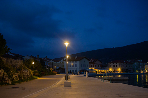 Cres, Croatia - October 24, 2022: The harbor of Cres in the night, street lamps, blue sky