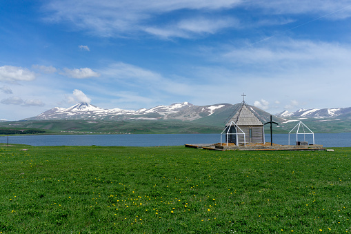 Small chapel near Paravani lake.  Natural lake, blue water, clouds, snowy 
mountains and blue sky. Located in Georgia.