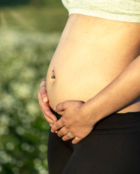 妊娠の最初の学期。妊娠初期の若い女性は、屋外で子供のコンセプトを待っています。自然の背景、コピー スペース - pierced abdomen flower beauty ストックフォトと画像