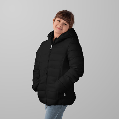 Mockup of a black winter puffer jacket on a child, garment zippers up, hands in pockets, front view, space for design, branding. Template fashionable streetwear, warm clothing, isolated on background.